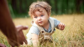 The little baby or year-old child on the grass in sunny summer day.